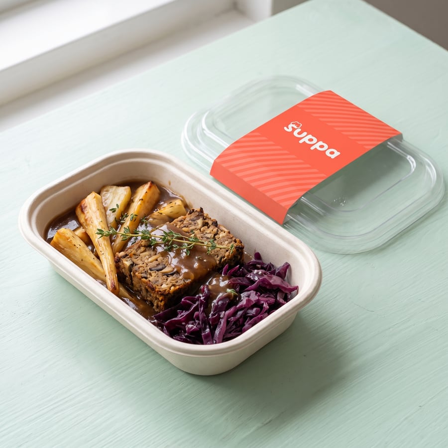 Chestnut and Mushroom Nut Roast in an open Suppa tray, with its clear lid and coral sleeve set beside it