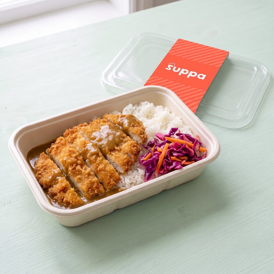 Chicken katsu curry in an open Suppa tray, with its clear lid and coral sleeve set beside it
