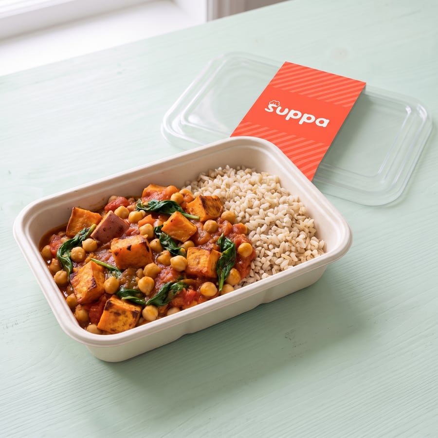 Chickpea and sweet potato curry in an open Suppa tray, with its clear lid and coral sleeve set beside it