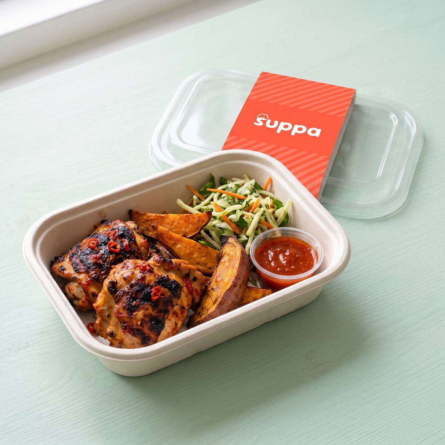 Piri piri chicken in an open Suppa tray, with its clear lid and coral sleeve set beside it